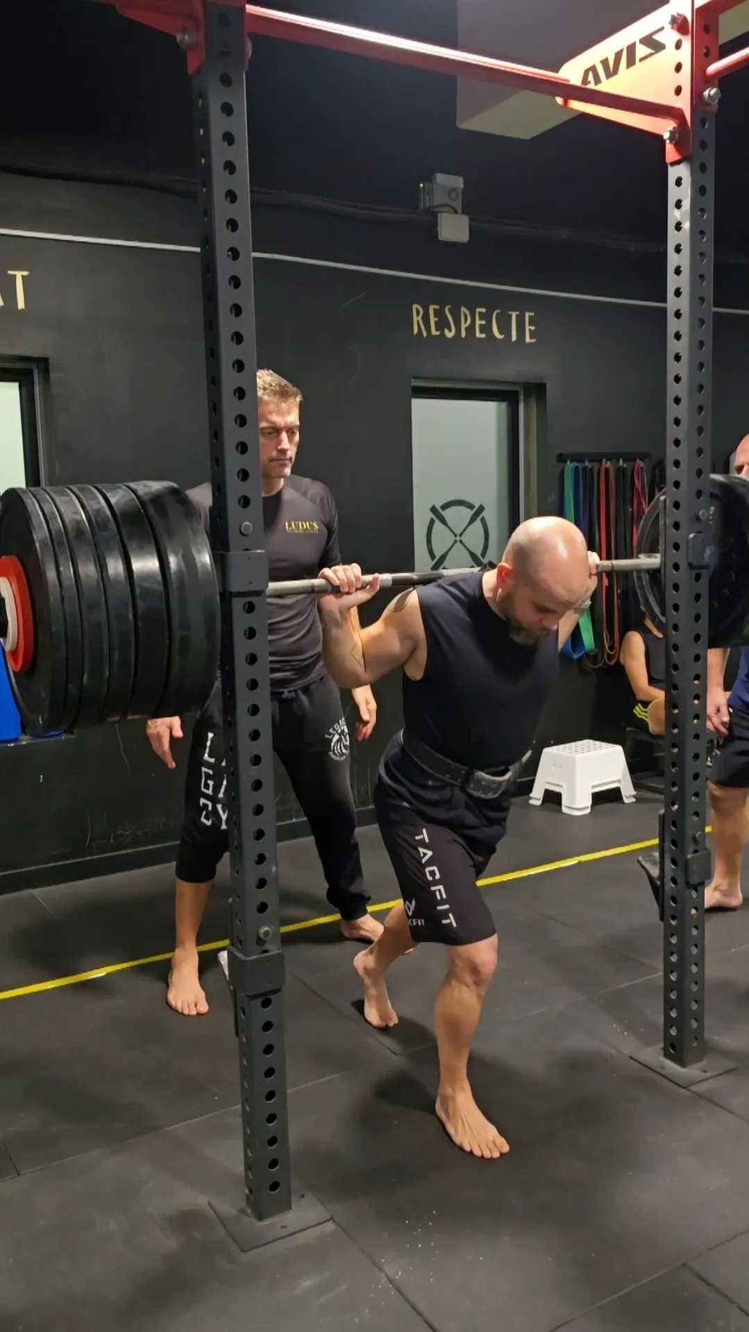 Entrenador de Ludus supervisando una sentadilla con barra en el rack
