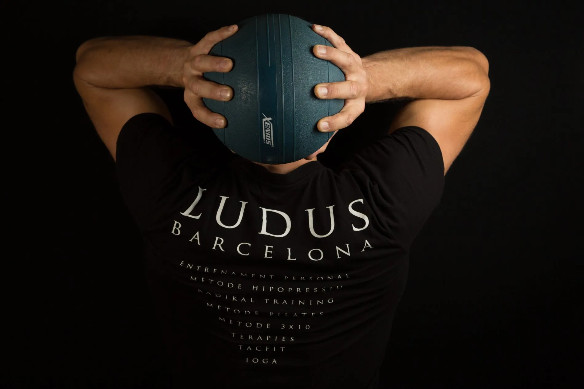 Alumno de Ludus sujetando un balón medicinal detrás de la cabeza